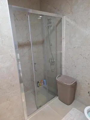 a glass shower stall with a trash can in a bathroom at Apartman L&S in Doboj