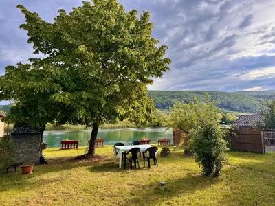 a table and chairs under a tree next to a lake at Guest House Seka in Bihać