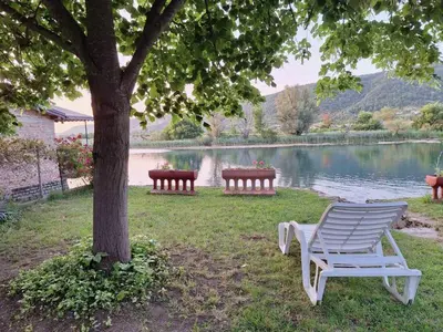 a white chair sitting under a tree next to a lake at Guest House Seka in Bihać