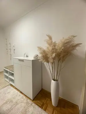 a white vase with flowers in the corner of a room at Apartman I&T in Banja Luka
