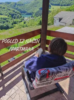 a boy sitting on a bench looking out over a valley at Domus Foresta Apartmani in Brdo