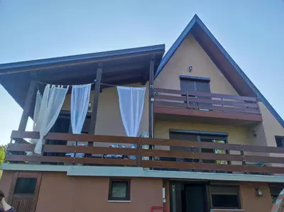 a house with a balcony with white curtains at Domus Foresta Apartmani in Brdo