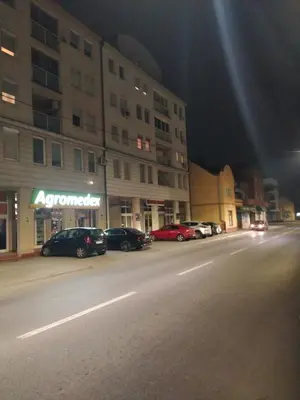 a city street at night with cars parked in a parking lot at GiV Apartman in Prijedor