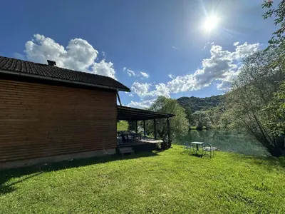 a building with a picnic table on the grass next to a lake at Vila kraljice Teute in Jezero