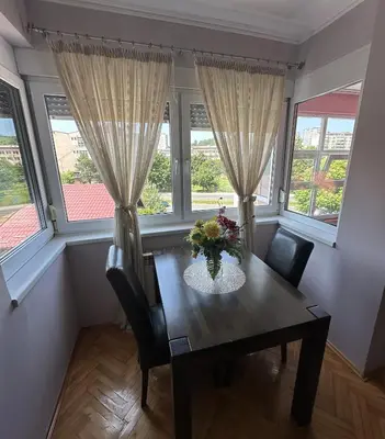 a dining room with a table and two windows at Apartment Bella - Tuzla, Mejdan in Tuzla