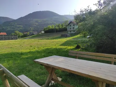 a wooden picnic table in a field with a house at Apartman Džanan in Jajce