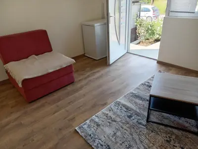 a living room with a red chair and a sliding glass door at apartman Tomić in Glamoč
