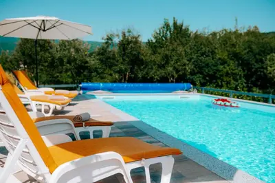 a swimming pool with lounge chairs and an umbrella at Velvet House Lohovo in Bihać