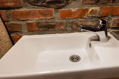 a white sink with a faucet next to a brick wall at Etno Camp Lucić in Odžak