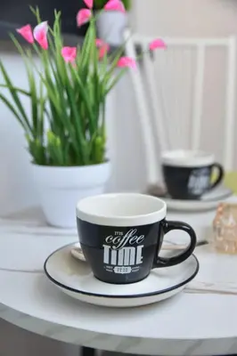 a coffee mug on a plate on a table with flowers at Apartman Sweet in Prijedor