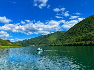 a man kayaking on a lake with mountains in the background at Kamp Glamp Plivska Oaza in Jajce