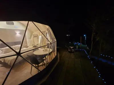 a tent with a table and chairs on a deck at night at Kamp Glamp Plivska Oaza in Jajce