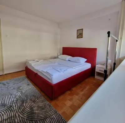 a bedroom with a red bed and a rug at MI apartman in Tuzla