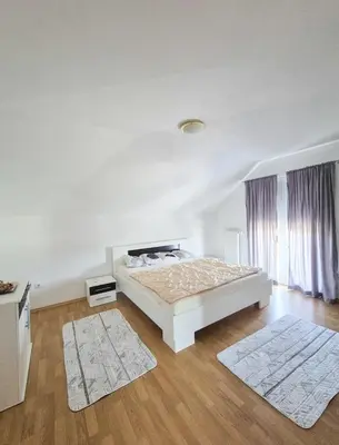 a white bedroom with a bed and two rugs at Wildlight in Bihać