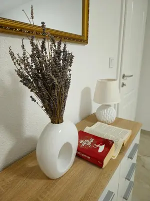 a white vase on a table with a book and a lamp at Apartman devet rijeka in Sanski most