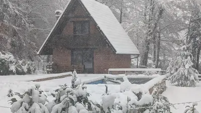 a house covered in snow in front at Dunja Cabin - Forest House with Pool in Banja Luka