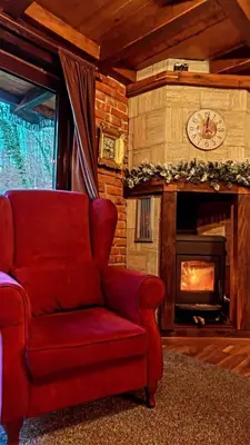 a red chair in a living room with a fireplace at Dunja Cabin - Forest House with Pool in Banja Luka