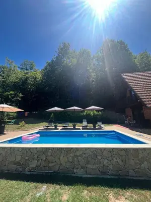 a swimming pool with chairs and umbrellas in a yard at Dunja Cabin - Forest House with Pool in Banja Luka
