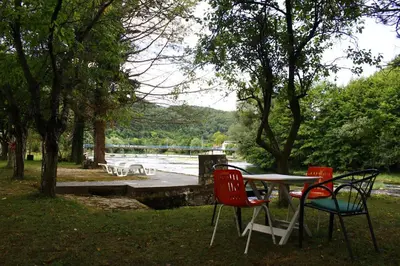 three chairs and a table in a park with a lake at River Nest in Kulen Vakuf