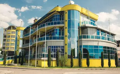 a yellow and blue building with trees in front of it at Hostel Fortuna in Banja Luka
