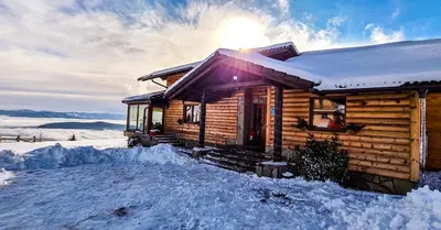 a log cabin in the snow with the sun shining at Planinska kuća 