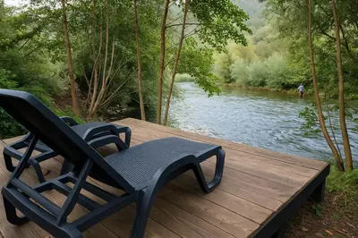 a black chair sitting on a wooden deck next to a river at River`s Song Cottage Jajce in Jajce