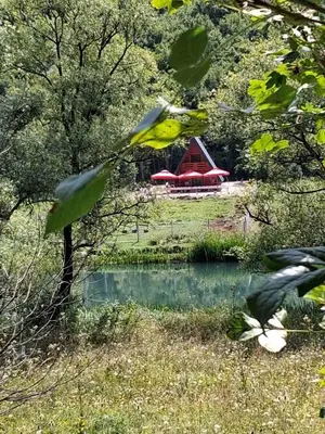 a red barn in the middle of a field with a pond at Whisper of the Pliva in Šipovo