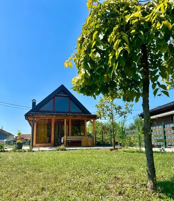a house with a black roof and a tree at Dabar kuca za odmor in Banja Luka