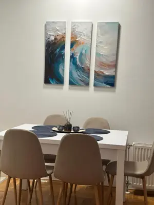 a dining room with a table and four paintings on the wall at Apartman Radmanović in Banja Luka