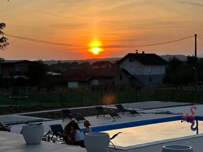 a group of people sitting around a swimming pool at sunset at Apartments Daisy in Banja Luka