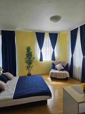 a bedroom with a bed and a couch and blue curtains at Rooms MIG in Banja Luka