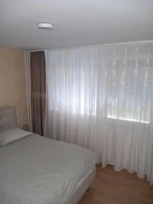 a bedroom with a bed and a window with white curtains at Apartman AM Tuzla in Tuzla