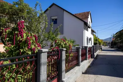 a fence in front of a house with pink flowers at Una Riverside Heritage House in Bihać