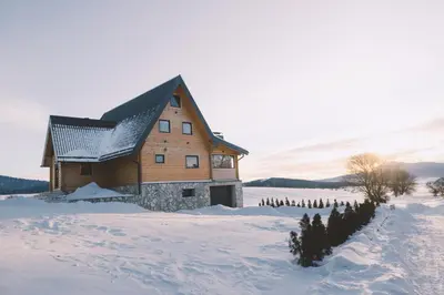 a large wooden building in a snowy field with trees at Villa Alba in Kupres