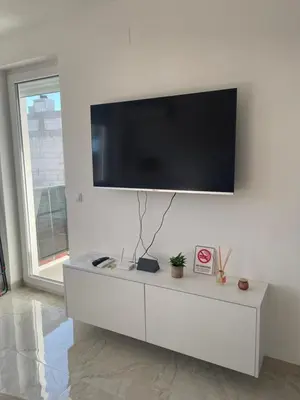 a white living room with a tv on a wall at Apartment Welcome in Modriča