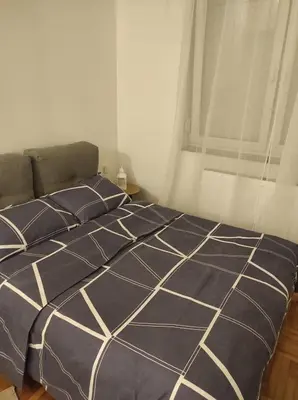 a bed with a blue and white comforter and a window at Studio Maja in Banja Luka