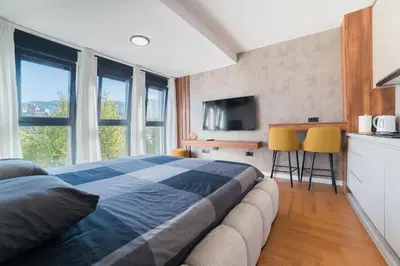 a bedroom with a bed and a kitchen with windows at Liberty Studio Tuzla in Tuzla