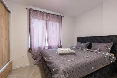 a bedroom with a bed with a purple comforter and a window at NolE Apartments in Visoko