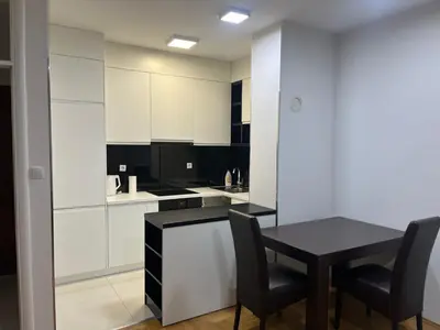 a kitchen with white cabinets and a black table and chairs at Apartman Dona in Banja Luka