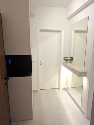 a white hallway with a door and a mirror at Apartman MYKA sa privatnim parkingom in Banja Luka