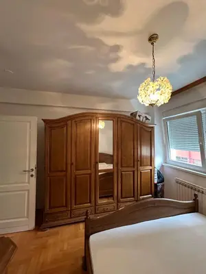 a bedroom with a wooden cabinet and a chandelier at KT Apartment City Centar in Banja Luka