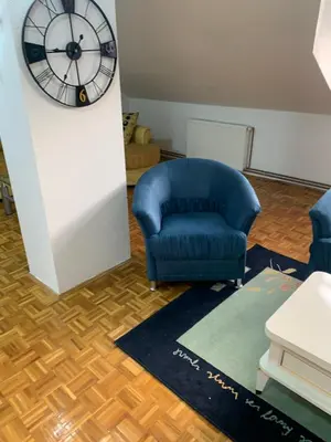 a living room with a blue chair and a clock at Vista Dubica in Bosanska Dubica