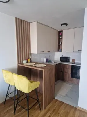 a kitchen with a counter and two yellow chairs at Apartman Green Oaza in Doboj