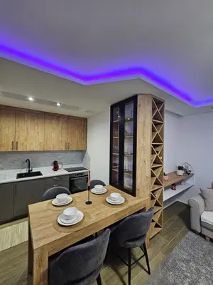 a dining room with a table and a kitchen with purple lighting at Apartman IVA in Modriča