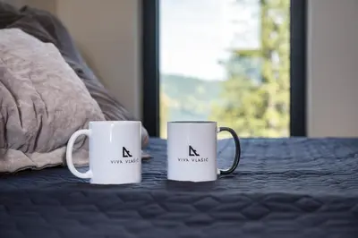 two white coffee mugs sitting on a bed at Viva Vlasic - Apartman i vikendica in Šišava