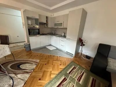 a kitchen with white cabinets and a wooden floor at Golden Lilly Apartment in Bihać