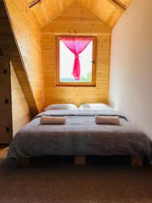 a bedroom with a bed with a window with a pink curtain at Brvnara Duga njiva Banjaluka in Čelinac