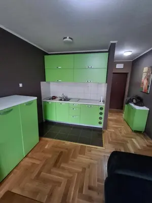 a kitchen with green cabinets and a wooden floor at Studio apartman in Banja Luka