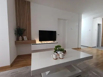 a white living room with a table and a tv at Apartman Home Away in Banja Luka