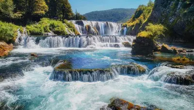 a river with waterfalls and rocks and trees at Apartman Mila in Bihać